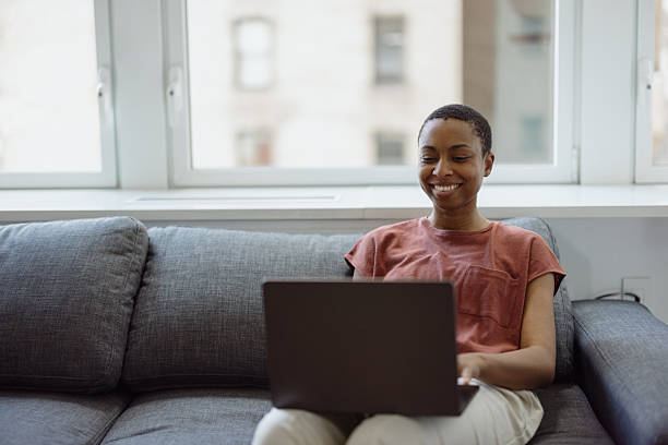 istock Young woman working from home sitting on sofa using laptop 2230251521