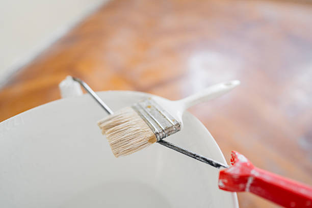 A paint brush on a paint bucket in an empty apartment under renovation.