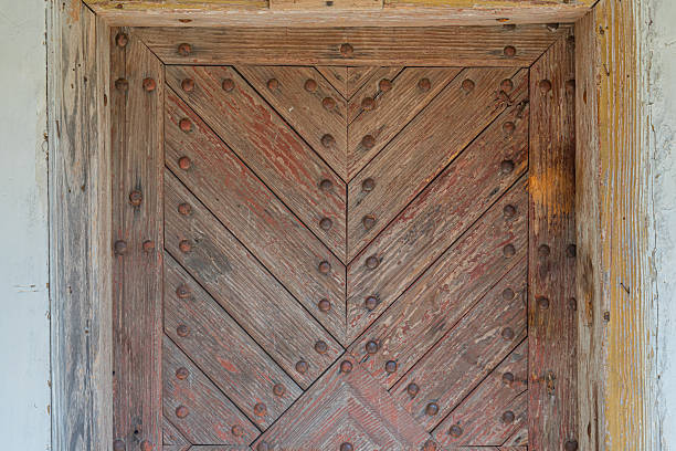 Age-worn wooden door in a Central European village Rectangular shape, symmetrical design with three sections, rough texture, randomly placed nails, subtle background structure hint, natural lighting