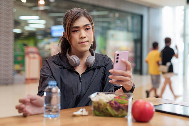 Transgender non binary woman using smartphone after training while having healthy meal indoors