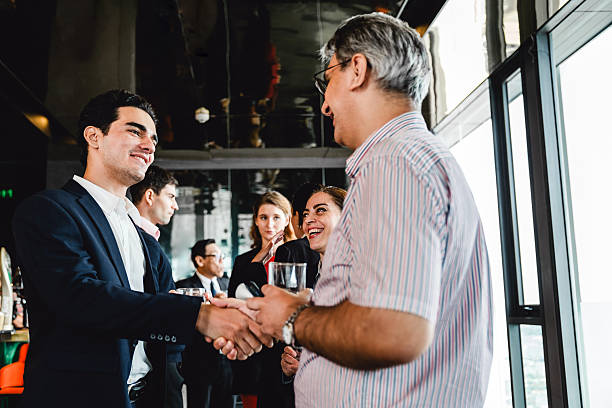 istock Businessman and colleague exchange a handshake during a casual networking event. Smiling professionals build new connections in a relaxed atmosphere with open conversations and drinks. 2230273498