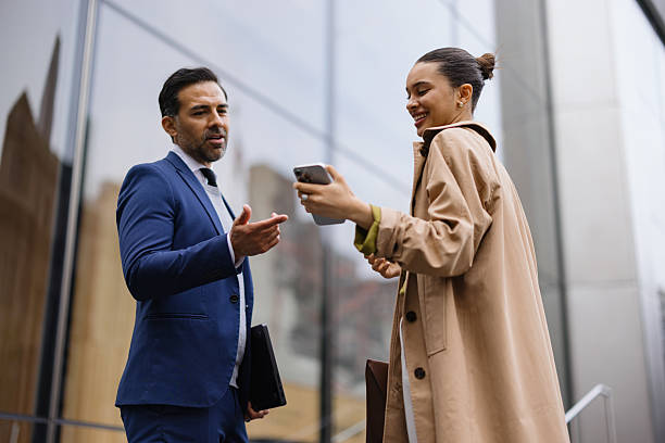 istock Business partners discussing a project using a smartphone in front of modern office buildings 2230273657