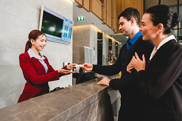 istock Smiling hotel receptionist hands key card to a couple during check-in at front desk. Warm service and guest interaction reflect excellent hospitality in a modern travel experience. Customer service 2230273661