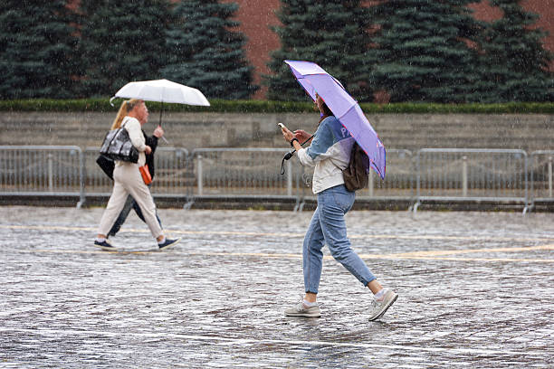 People with umbrellas walking on the Red Square in Moscow during heavy rain stock photo