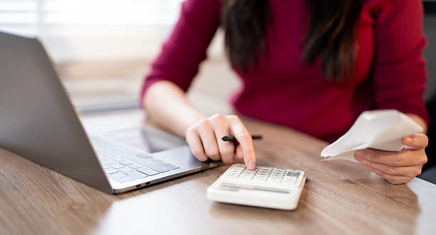 istock A woman is using a calculator and holding a receipt, while working on a laptop. 2230274327