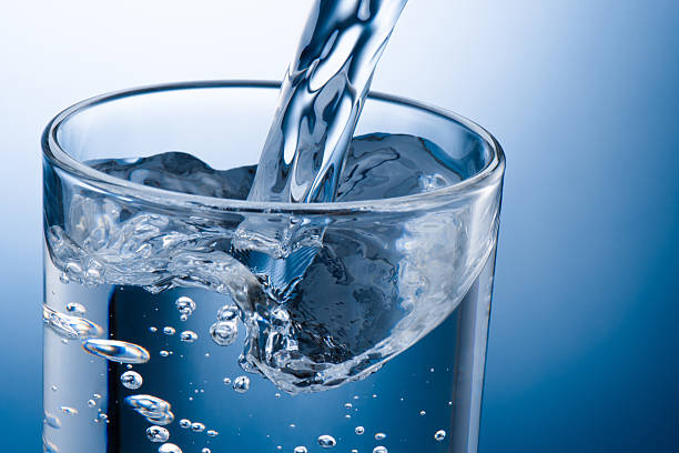 istock Pouring water into glass on blue background 2230275925