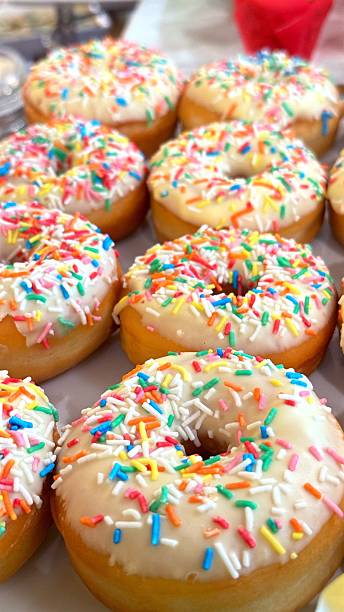Glazed donuts arranged appetizingly, featuring colorful sprinkles and white frosting, presenting irresistible bakery confections arranged on rustic wooden surface