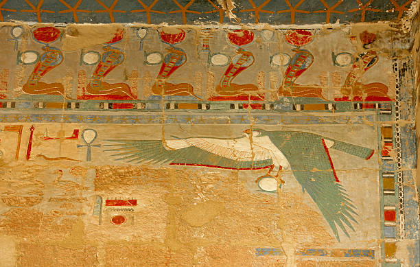 Colorful ancient Egyptian wall painting depicting the winged sun disk flanked by cobras wearing solar crowns, along with hieroglyphic inscriptions, from Luxor Temple, Egypt.