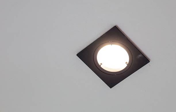 istock A square recessed light with a round light source is elegantly placed in the corner of a white ceiling. The black body of the light fixture creates a geometric contrast, and its bright light illuminates the space. 2230298240