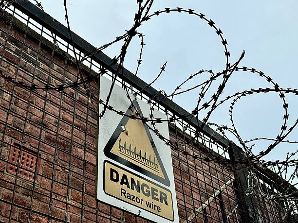 istock Low angle view of a barbed razor wire boundary with a danger warning sign with a tall brick building in the background at Blyth in Northumberland 2230308256