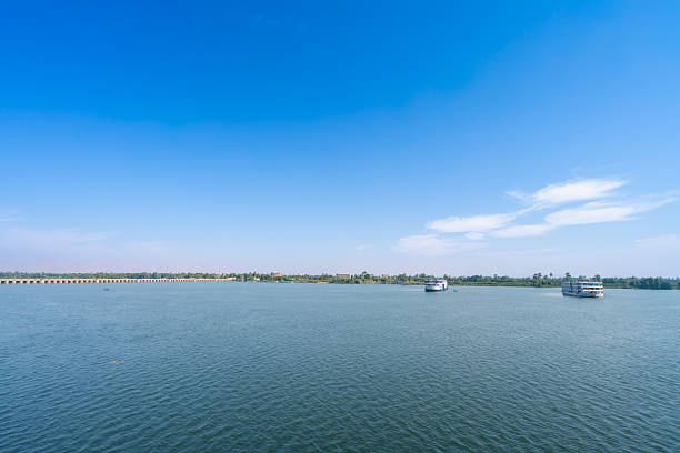 Wide panoramic view of Nile River with cruise ships and bridge near Esna Lock Egypt under beautiful blue sky with white clouds.