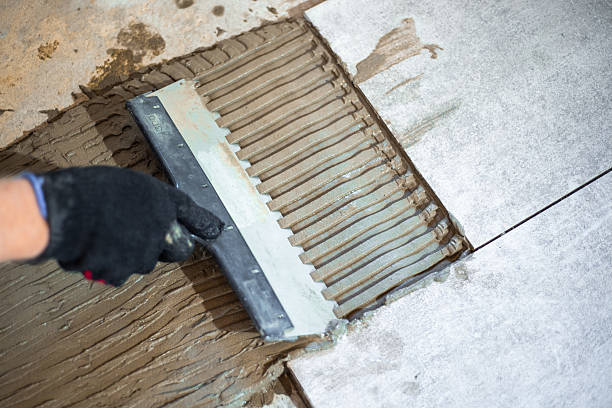 istock Applying tile adhesive with a notched trowel to the floor before laying large-format tiles 2230316966