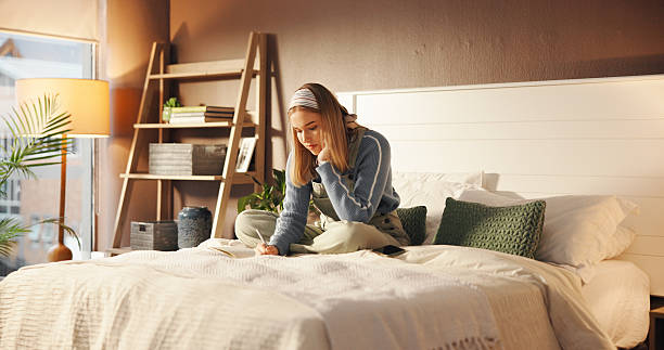 istock Girl, student and writing in notebook on bed for academic planning, study calendar or test reminder. Personal diary, person and taking notes in home for assignment schedule and weekend productivity 2230317415