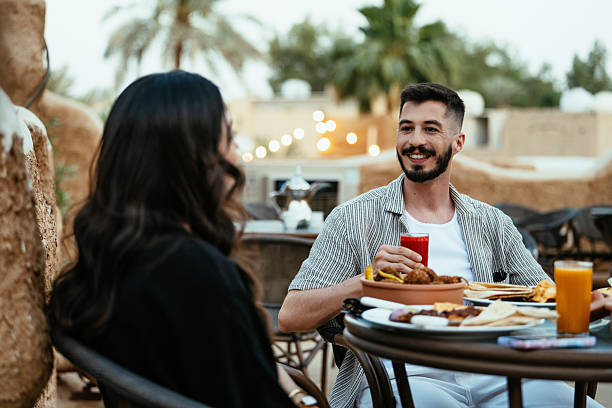 istock Rooftop restaurant setting with young heterosexual couple enjoying a meal, featuring traditional Middle Eastern clothing and architecture. 2230319152