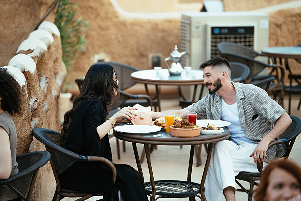 istock Rooftop restaurant setting with diverse people enjoying a meal, featuring traditional Middle Eastern clothing and architecture. 2230319183