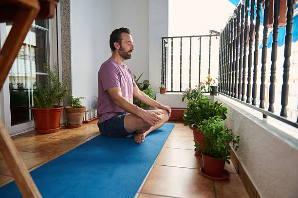 istock Man Practicing Meditation on Balcony Surrounded by Green Plants 2230327394