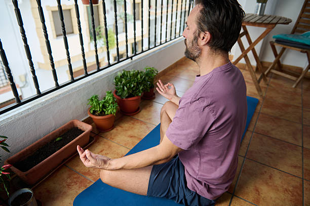 istock Man Practicing Meditation on Balcony with Yoga Mat and Potted Plants 2230327408