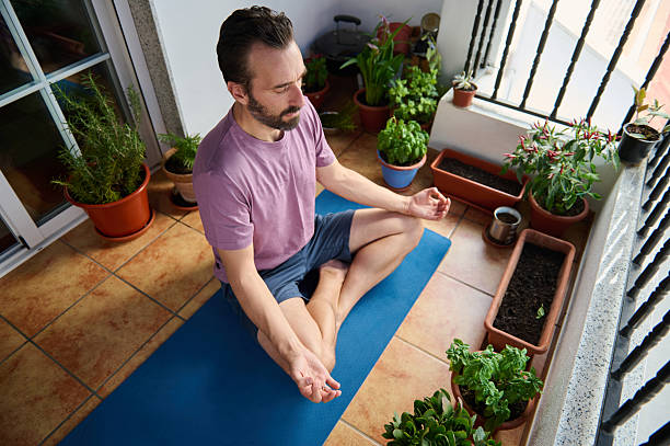 istock Man Meditating on Balcony Surrounded by Lush Potted Plants 2230327412