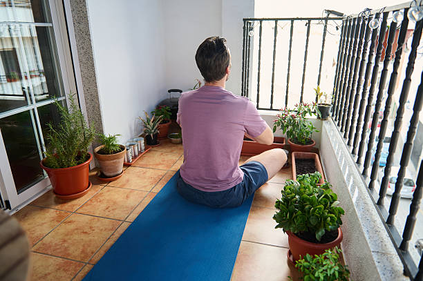 istock Man Practicing Relaxation on Balcony with Yoga Mat and Plants Displayed 2230327413