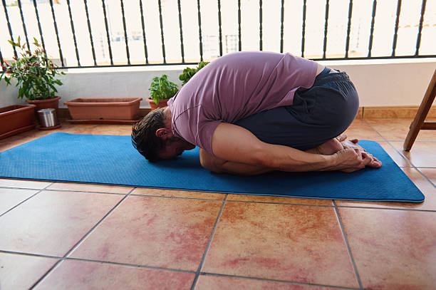 istock Man Practicing Child's Pose on Yoga Mat Outdoors on Home Balcony 2230327417