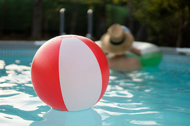 A vibrant, multicolored beach ball floats on the surface of a sparkling blue swimming pool under bright sunlight. This cheerful summer image evokes relaxation, playfulness, and vacation vibes — perfect for themes related to fun in the sun, poolside living, and outdoor leisure.
