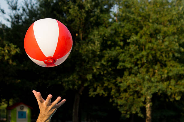 A woman's hand playing with a red and white beach ball