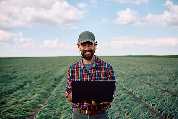 istock Happy agriculturist using laptop while working in the field and looking at camera. 2230336065