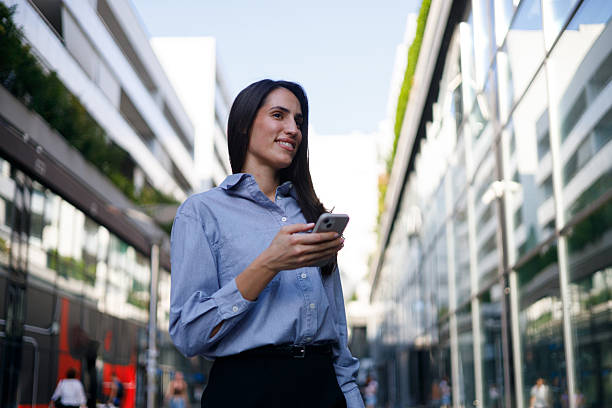 istock Professional businesswoman texting on smartphone while walking, cityscape background 2230337910