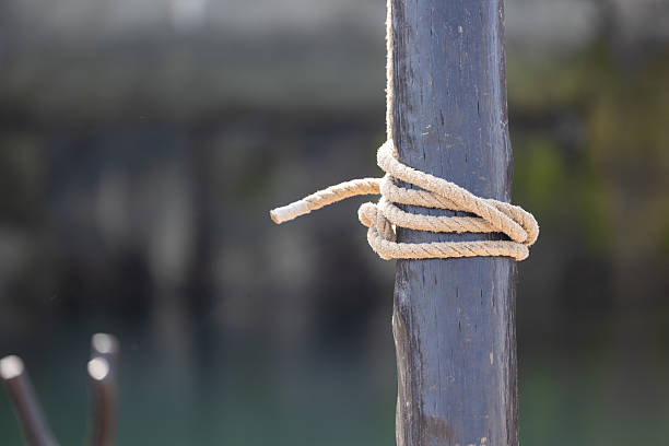 Hemp rope wrapped around a weathered wooden post near a body of water, providing a secure mooring