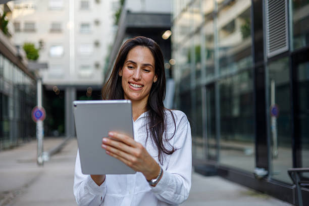 istock Young businesswoman using a digital tablet and smiling while walking outdoors in a business district 2230342008