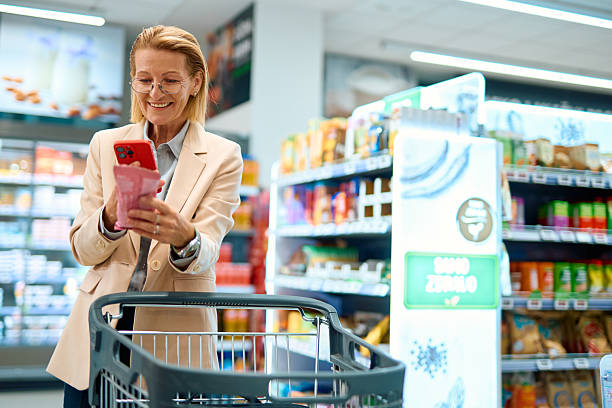 istock Smiling mature woman using smartphone while shopping in supermarket 2230345667