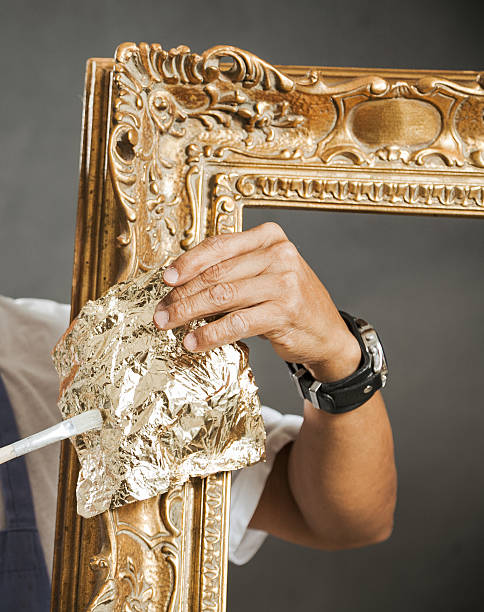 Craftsman applying gold leaf to antique picture frame