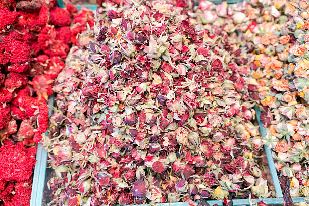 A close-up view of a market display filled with dried rosebuds in pink and cream tones, often used for tea, potpourri, or natural remedies.
