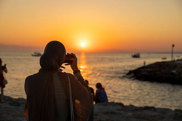 Female tourist photographing ocean view during sunset