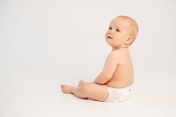 Curiosity and calmness. Beautiful little baby girl, toddler in diaper standing on bed with calm expression, isolated on white studio background. Concept of childhood, motherhood, care