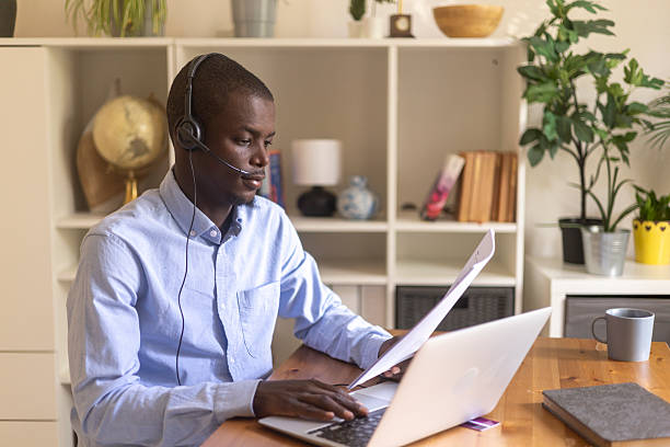istock Remote worker wearing headphones, reviewing paperwork while typing on computer keyboard 2230387476