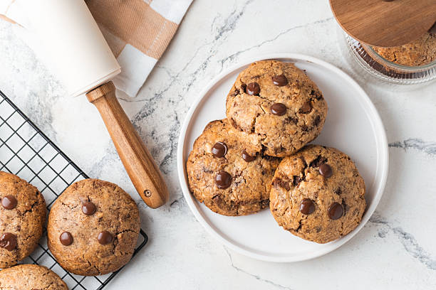 istock Fresh chocolate American chip cookies with nuts and chocolate drops on white marble background. Flat lay of cookies with stylish cutlery and pastry chef accessories. Recipe of homemade cookies concept 2230391126