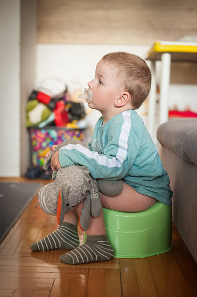 istock Young child sits on potty with toy and pacifier in bright indoor setting 2230391715