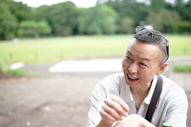A middle-aged Asian man sitting on a bench in the background talking.