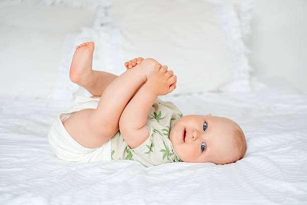istock a baby boy plays with his legs while lying on his back on a white bed at home, a smiling little child with blue eyes on the bed 2230393522