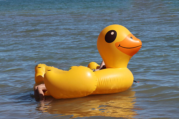 Legs of a tourist relaxing on an inflatable yellow duck floating on blue water