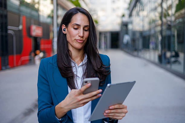 istock Businesswoman wearing wireless earbuds is using smartphone and digital tablet while walking outdoors 2230402580