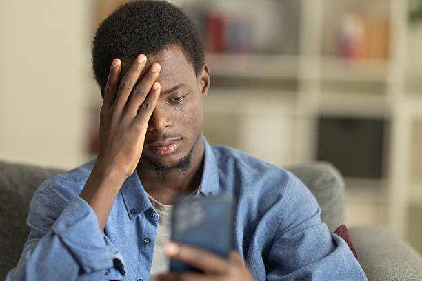 istock Frustrated young man covering face with hand while reading bad news on smartphone, sitting on sofa at home 2230406401