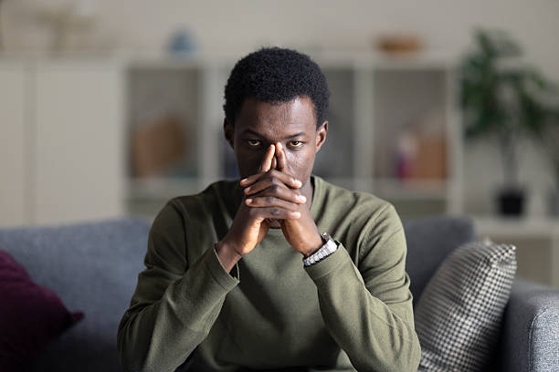 istock Pensive young man sitting on sofa at home, thinking with hands on chin 2230406606