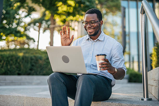 istock Young businessman waving during a video call on his laptop while holding a coffee 2230407553