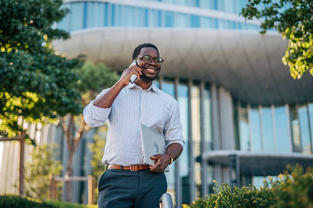 istock Smiling businessman talking on phone holding laptop in urban setting 2230407638