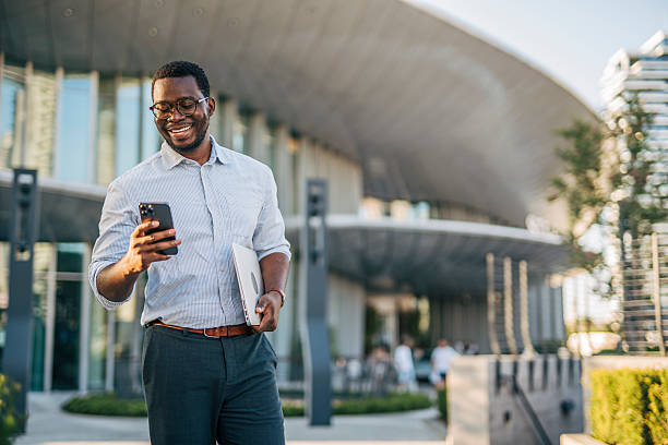 istock Smiling businessman using smartphone walking near office building 2230407913