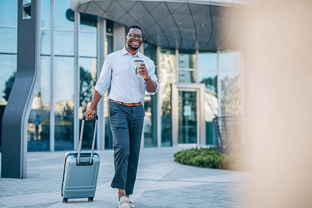 istock Smiling businessman walking with suitcase and coffee outside modern office building 2230408228