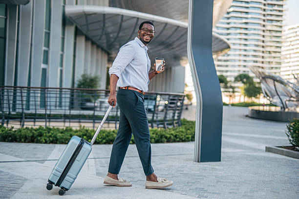 istock Smiling businessman walking with suitcase and coffee outside office 2230408255