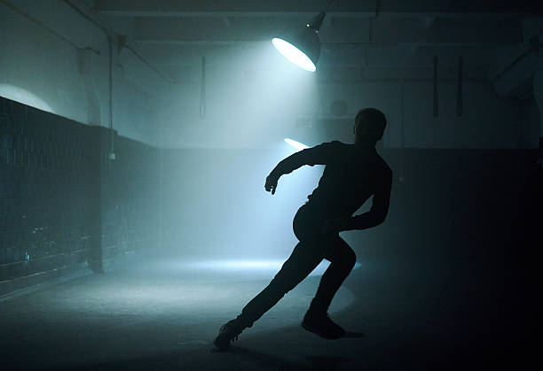 Art photo of a woman with a flowing dress on an asphalt road. She is backlit and is only recognizable as a rough silhouette due to the blurring. She is standing and yet appears to be falling. Everything is moving.